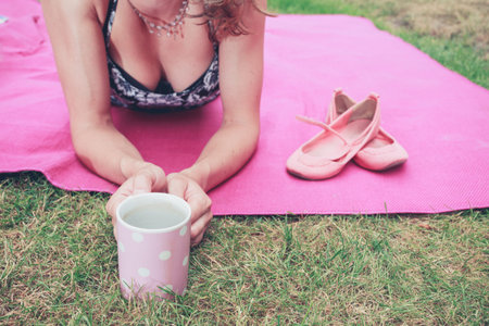 A young woman is sitting on a blanket on the grass and is having a cup of teaの写真素材