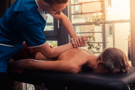 A massage therapist is treating a female client on a table by the windowの写真素材