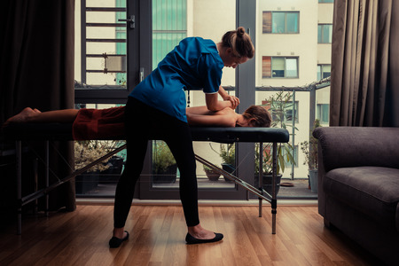 A massage therapist is treating a female client on a table in an apartment A massage therapist is treating a female client on a table in an apartment