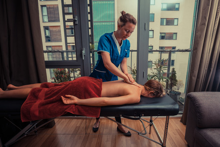 A massage therapist is treating a female client on a table in an apartmentの写真素材