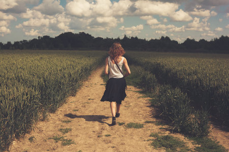 A young woman is walking along a track in the middle of a wheat field in summerの写真素材