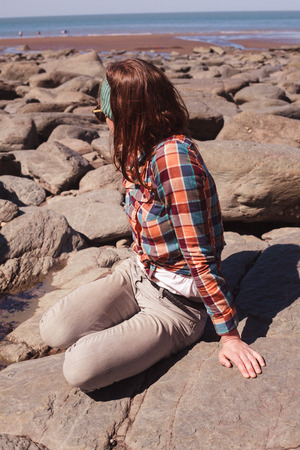 A young woman is sitting on a rocky beachの写真素材