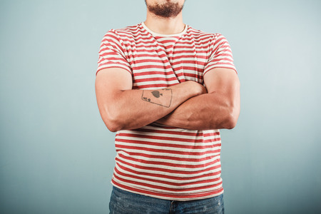 A young man with a tattoo is wearing a striped shirt and standing with his arms crossedの写真素材
