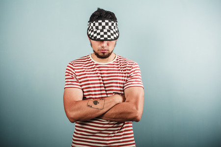 A young man with a tattoo is wearing a striped shirt and standing with his arms crossedの写真素材