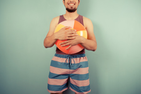 A happy young man wearing a vest is holding beach ballの写真素材