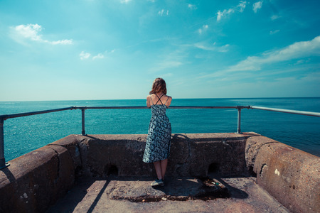 A young woman is standing at the end of a pier by the oceanの写真素材