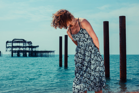 A young woman is standing by the ocean with an old derelict pier in the backgroundの写真素材