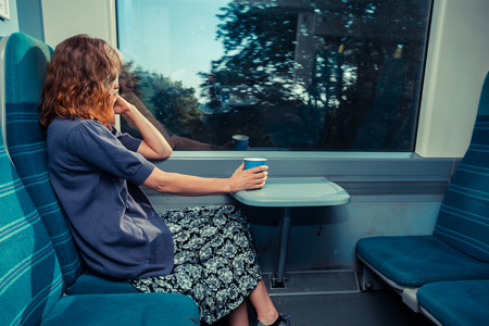 A young woman is sitting on a train with a cup of coffee and is looking outの写真素材