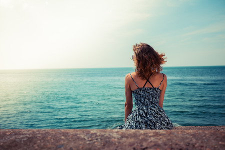 A young woman is sitting on a pier by the oceanの写真素材