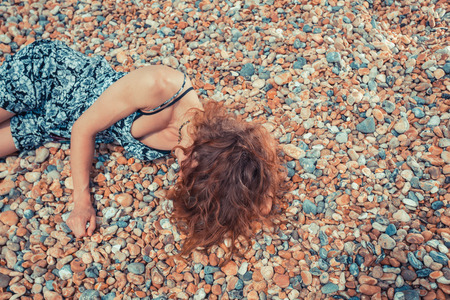 A young woman is lying on a pebble beachの写真素材