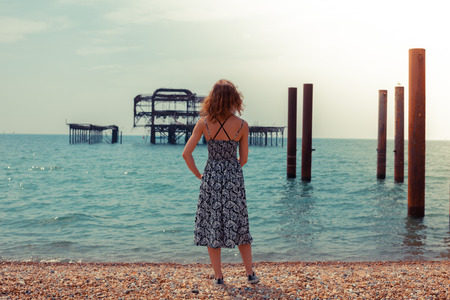 A young woman is standing by the ocean with an old derelict pier in the backgroundの写真素材
