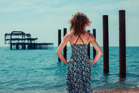 A young woman is standing by the ocean with an old derelict pier in the backgroundの写真素材