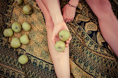 A young woman is sitting on a blanket and holding some applesの写真素材
