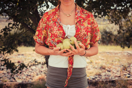 A young woman is standing under a tree and is holding a bunch of applesの写真素材