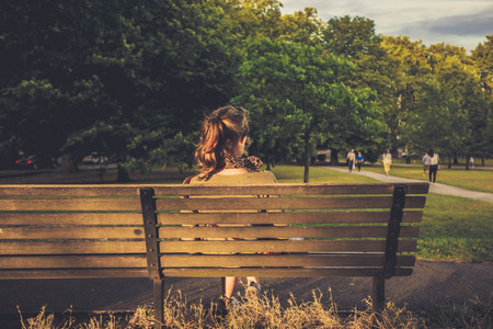 A young woman is relaxing on a bench at sunsetの写真素材