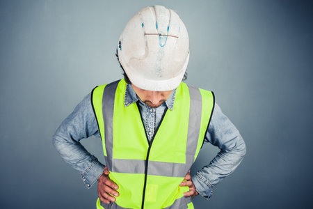 A young engineer in hard hat and high vis is looking down