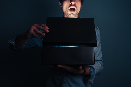 A young man is opening a box with something exciting inside itの写真素材