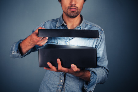 A young man is opening a box with something exciting inside itの写真素材