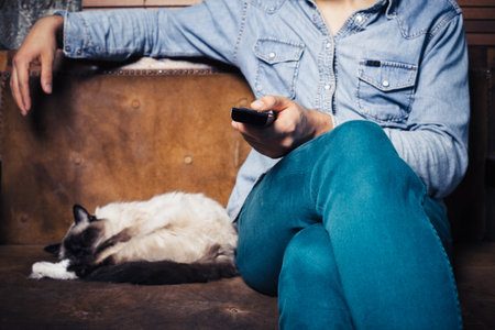 A young man is sitting on a sofa with a cat and is watching television