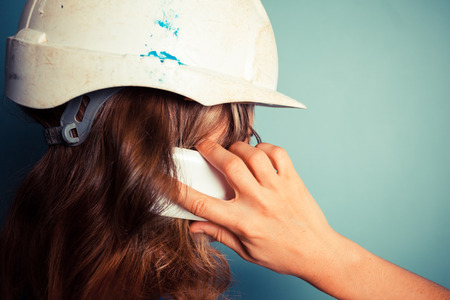 A young female builder wearing a hard hat is talking on the phoneの写真素材