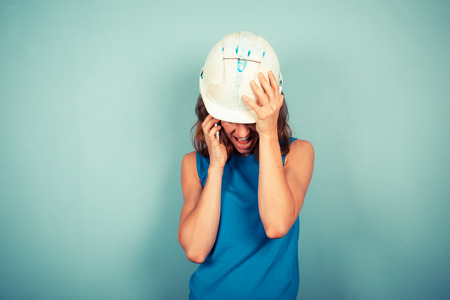 A young female builder wearing a hard hat is talking on the phoneの写真素材