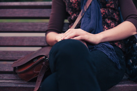A young woman is sitting on a park bench in the autumnの写真素材