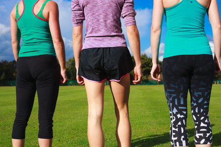 Three women wearing sportswear are standing in the park on a sunny day