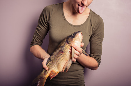 A young woman is posing with carp and is pulling silly facesの写真素材