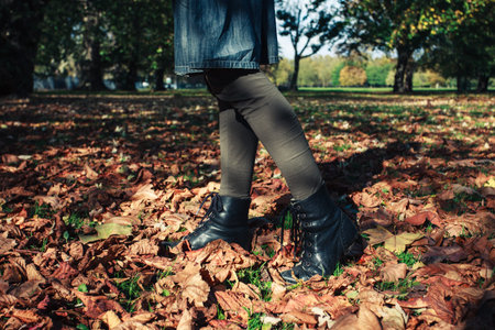 The legs of a woman as she is walking in fallen leaves in the park