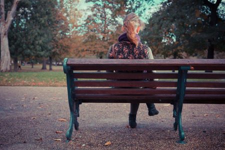 Rear view of a young woman sitting on a park bench in autumnの写真素材