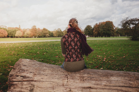 A young woman is stitting on a large fallen tree in the park on a sunny autumn dayの写真素材