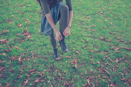 A young woman is tying her shoe in the park on the grassの写真素材