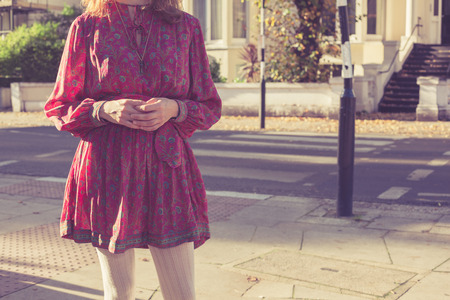 A young woman is standing in the street in a residential area of the city on a sunny dayの写真素材