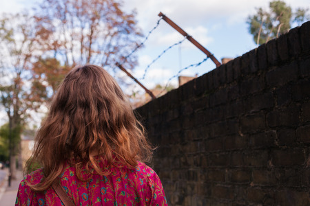 A woman is standing by a wall with barb wireの写真素材