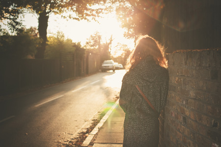A young woman is walking into the sunset on an autumn day in the cityの写真素材