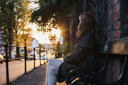 A young woman is sitting on a bench at sunset on an autumn day in the cityの写真素材