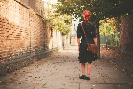 A young redhead woman is walking in a cobbled alley in the autumn on a sunny dayの写真素材