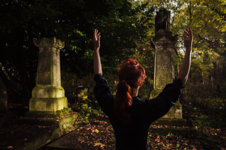 A redhead woman or witch is raising her arms and performing a ritual by a graveの写真素材