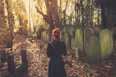 A young woman is walking amongst the tombstones in a cemeteryの写真素材