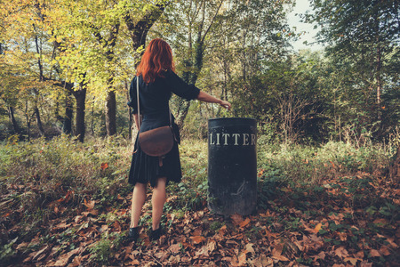 A young woman is putting something in a bin in the forestの写真素材