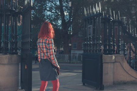 A young woman is standing by the gates of a park on a sunny autumn dayの写真素材