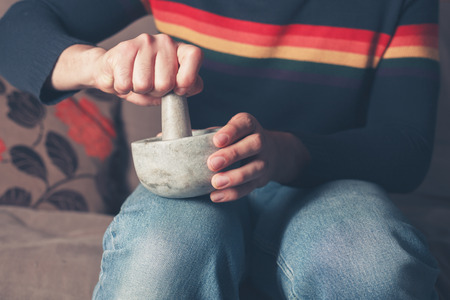 A young man is sitting on a sofa and is grinding pepper with a pestle and mortarの写真素材