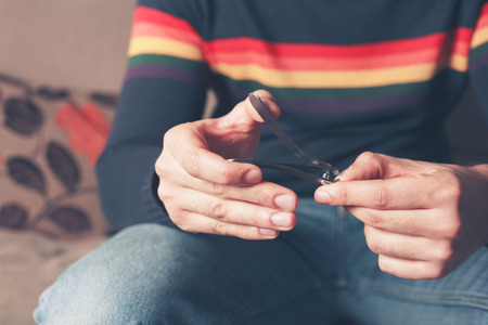 A young man is sitting on a sofa and is clipping his finger nailsの写真素材