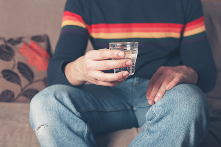 A young man is sitting on a sofa with a glass of water in his handの写真素材