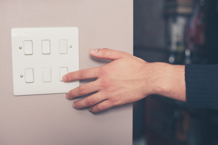 A young man's hand is switching on a light switch at homeの写真素材