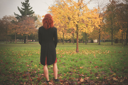 A young woman is standing by a tree in the park in autumnの写真素材