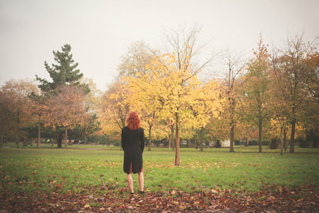 A young woman is standing by a tree in the park in autumnの写真素材