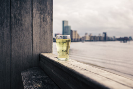 A glass of beer on a wooden terrace by a river in the cityの写真素材