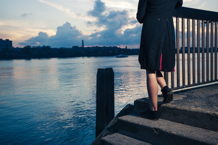 A young woman is stading on some stairs by a river at sunsetの写真素材