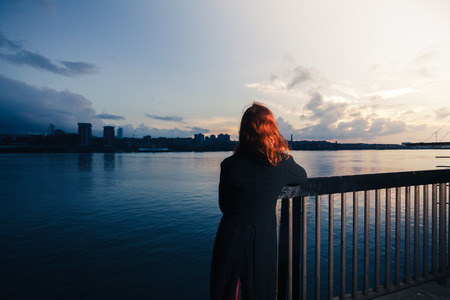 A young woman is admiring the sunset over a river in the cityの写真素材